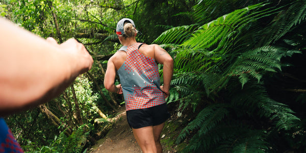 Runner in a patterned Fractel singlet and cap on a fern-lined trail from the butterfly effect running collection