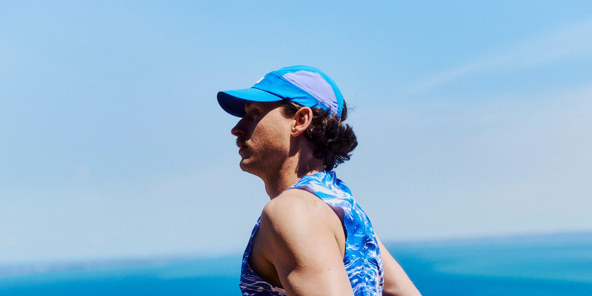 Runner in a bright blue Fractel race day running cap and patterned singlet against blue sky and sea