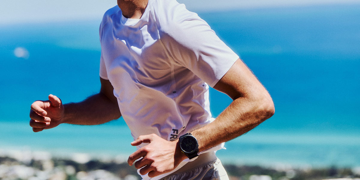 Runner in a white Fractel tee from our range of running shirts, with the ocean behind him