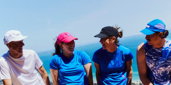 Four runners in Fractel running shirts and caps on a hilltop by the sea, showing womens running tops in bright blue