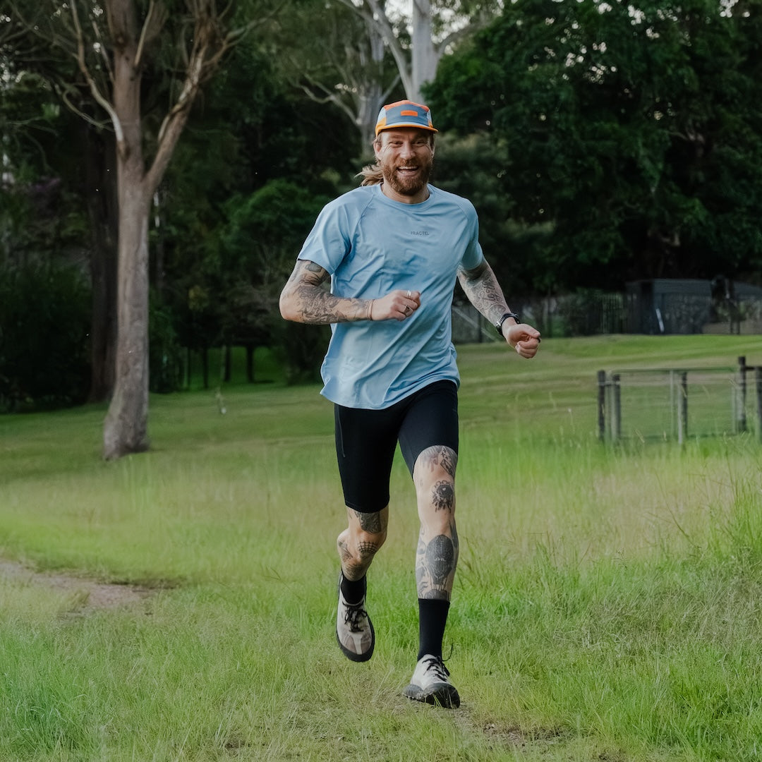 Man running in blue shirt on a grassy path with trees in the background