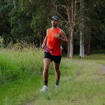 Man running in orange singlet in a grassy field 