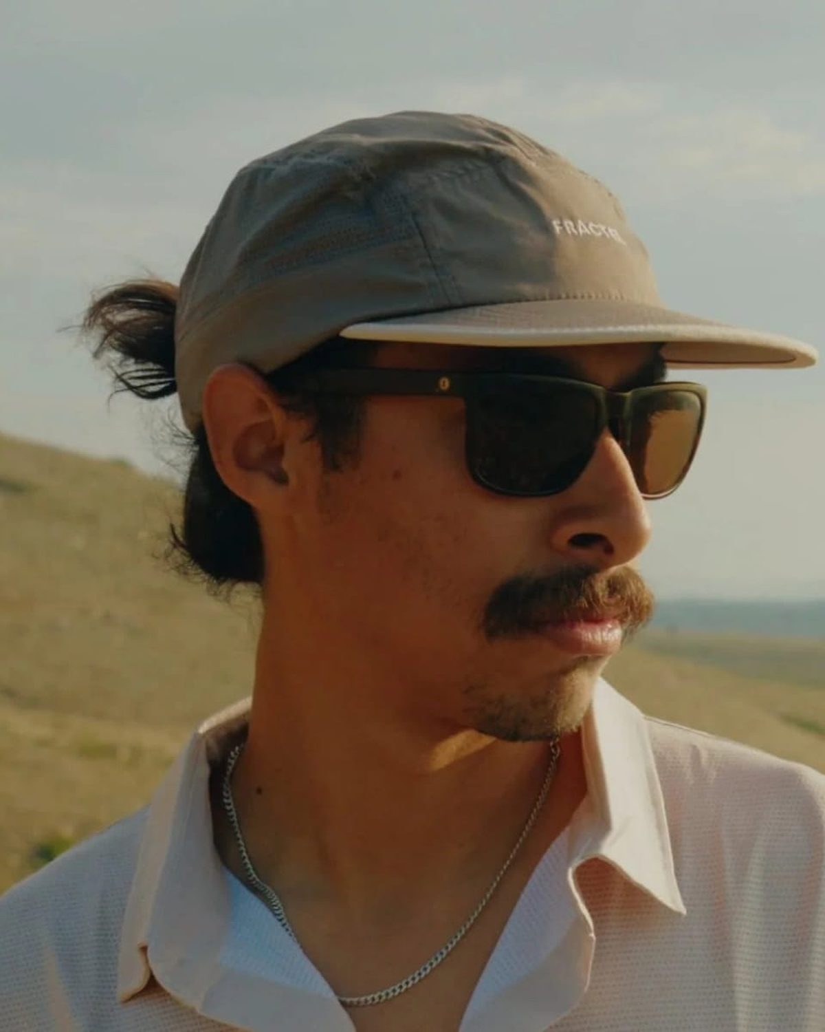 Grey Fractel running cap worn by a runner in sunglasses on a grassy hillside